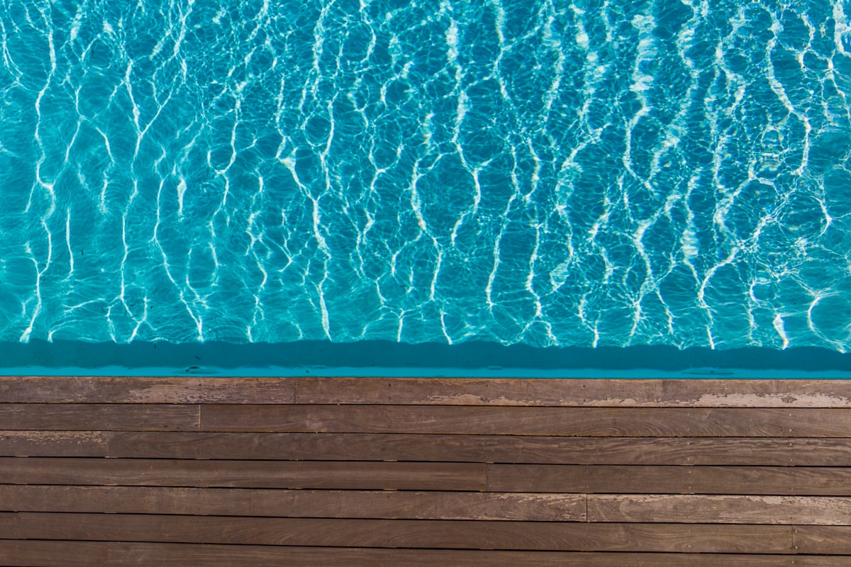 Sunlight rippling through crystal-clear balanced pool water beside a timber deck