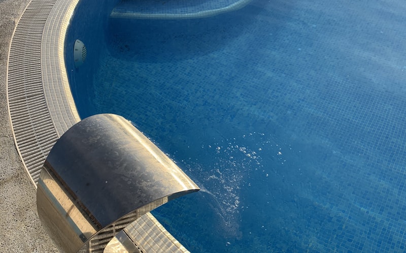 Filtered water returning into a blue mosaic pool through a stainless spillway
